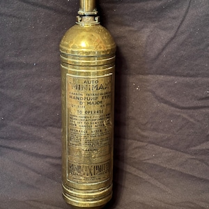 Peut inclure: Extincteur à pompe manuelle Auto Minimax en laiton vintage. Il comporte une poignée et une étiquette avec des instructions. L'étiquette indique "Carbon Tetrachloride" et "Minimax Limited", un fabricant britannique.