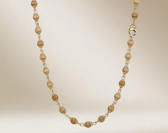 May include: A gold-toned necklace featuring small, light brown, barrel-shaped beads strung together with delicate gold chain links. The necklace has a simple clasp closure and hangs against a soft, neutral background.