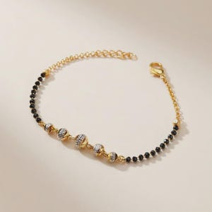May include: A gold-coloured bracelet with black beads and decorative gold and silver-toned spheres. The bracelet has a delicate chain and a lobster clasp. The design is elegant and suitable for various occasions.