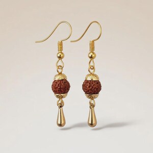 May include: A pair of gold-colored earrings. Each earring features a brown, textured bead, a gold-colored cap, and a teardrop-shaped charm. The earrings have a simple hook design.