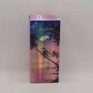 Puede incluir: Caja rectangular de spray de perfume Calgon Tropical Dream Intense. La caja presenta una escena de puesta de sol tropical con palmeras y las palabras "NEW" y "CALGON". Contiene 44 ml.