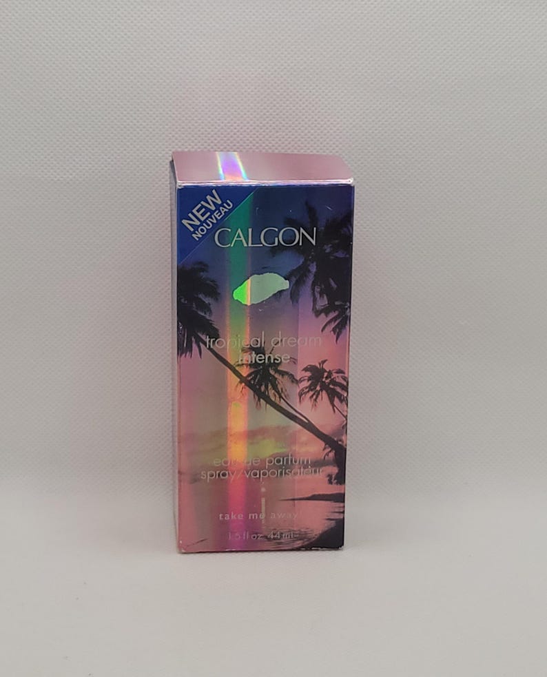 Puede incluir: Caja rectangular de spray de perfume Calgon Tropical Dream Intense. La caja presenta una escena de puesta de sol tropical con palmeras y las palabras "NEW" y "CALGON". Contiene 44 ml.