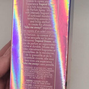 Puede incluir: Una caja rosa e iridiscente de Calgon Tropical Dream Eau de Parfum Spray. La caja presenta texto que describe las notas de mandarina, maracuy&aacute; y carambola. La marca y el logotipo son visibles.