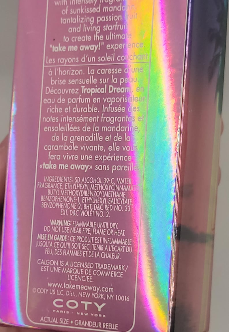 Puede incluir: Una caja de perfume con un acabado hologr&aacute;fico iridiscente. El texto en la caja incluye "Tropical Dream" y "take me away!" en ingl&eacute;s y franc&eacute;s. La caja es de color rosa y morado.