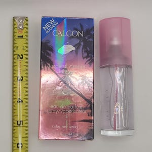 Puede incluir: Un frasco de spray de eau de parfum Calgon Tropical Dream Intense con tapa rosa y caja a juego. La caja presenta una escena tropical con palmeras y el texto "NEW NOUVEAU". El frasco es de 44 ml.