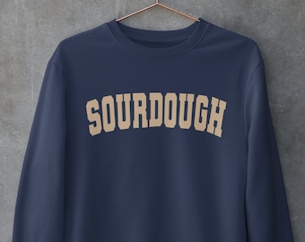 May include: A navy blue sweatshirt with the word "SOURDOUGH" printed in a beige color across the chest.