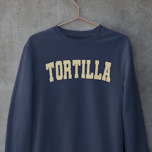 Puede incluir: Una sudadera azul marino con la palabra "TORTILLA" impresa en color crema en el pecho.