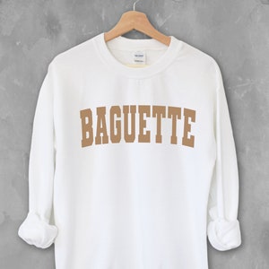 May include: White sweatshirt with a brown graphic that says "BAGUETTE" in a collegiate font.