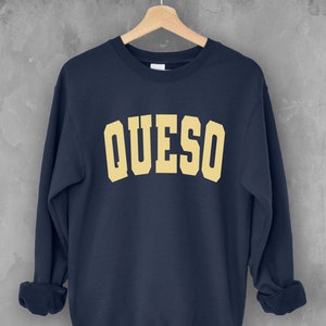 May include: A navy blue sweatshirt with the word "QUESO" printed in a yellow color on the front.