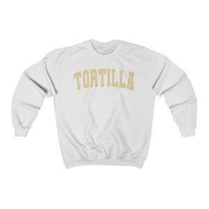 Puede incluir: Sudadera blanca con la palabra "TORTILLA" impresa en un arco dorado en el pecho.