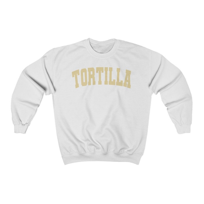 Puede incluir: Sudadera blanca con la palabra "TORTILLA" impresa en un arco dorado en el pecho.
