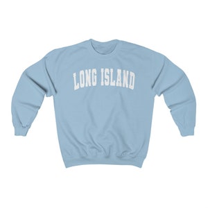 Puede incluir: Una sudadera de color azul claro con el texto "LONG ISLAND" impreso en blanco en la parte delantera.