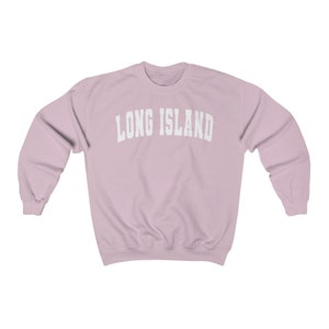 Puede incluir: Una sudadera de color rosa claro con el texto "LONG ISLAND" en blanco, en letras arqueadas.