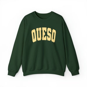 May include: A dark green sweatshirt with the word "QUESO" printed in a yellow-gold color across the chest.