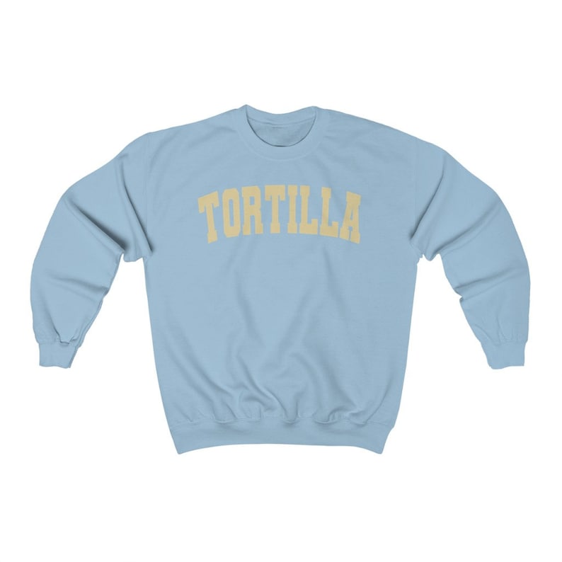 Puede incluir: Una sudadera azul claro con la palabra "TORTILLA" impresa en un arco amarillo sobre el pecho.