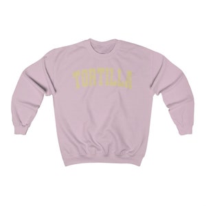 Puede incluir: Una sudadera de color rosa claro con la palabra "TORTILLA" impresa en amarillo en el pecho.