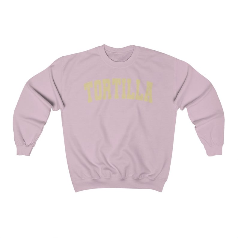 Puede incluir: Una sudadera de color rosa claro con la palabra "TORTILLA" impresa en amarillo en el pecho.