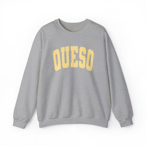May include: A gray sweatshirt with a yellow arch design that says "QUESO" on the front.