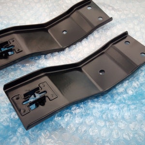 May include: Two black metal brackets with a curved shape and multiple holes. The brackets are on a blue background.
