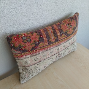 Op de afbeelding: Rechthoekig decoratief kussen met een vintage patroon. Het bovenste gedeelte heeft een rood, bordeauxrood en goudkleurig bloemenpatroon, terwijl de onderkant een beige en roze geometrisch ontwerp heeft. Het kussen heeft een zwarte achterkant.