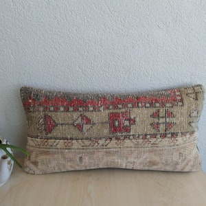 Könnte beinhalten: Rechteckiges beiges Kissen mit gewebtem Design. Das Kissen hat ein zentrales Band mit roten und braunen geometrischen Mustern. Der untere Bereich hat ein helleres, strukturiertes Beige. Ideal für die Inneneinrichtung.