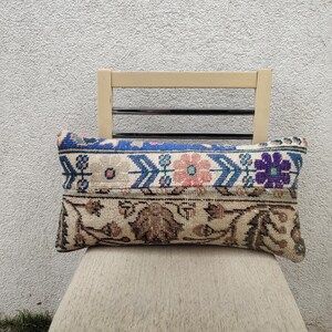 May include: A rectangular cushion with a floral and geometric pattern. The top section features blue, pink, and purple floral designs, while the bottom section has a brown, beige, and tan pattern. The cushion is resting on a beige chair.
