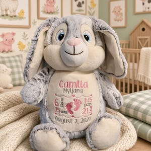May include: A plush gray rabbit toy with long ears and a cream-colored belly. The belly features embroidered text reading Camilla Myljana, 6 lbs 7.5 ozs, 1:45 pm, 21 inches, and August 2, 2021, alongside two pink baby footprint icons.