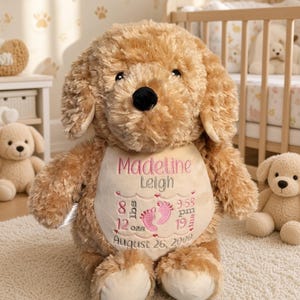 May include: A plush tan dog toy with a cream-colored belly patch embroidered with the name Madeline Leigh, birth details including 8 lbs 12 ozs, 9:58 pm, 19 ins, the date August 26, 2000, and two small pink baby footprints in the center.