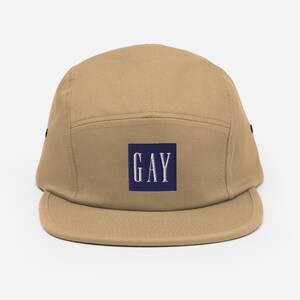 May include: A tan 5-panel cap with a navy blue square patch that says "GAY" in white lettering.