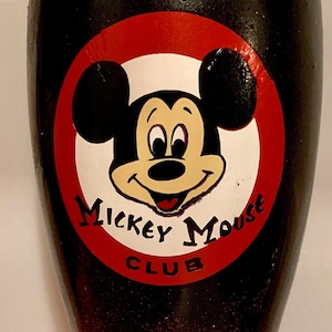 May include: A black and red glitter tumbler with a white Mickey Mouse design. The design includes Mickey Mouse's face with the words "Mickey Mouse Club" around it. The bottom of the tumbler has two white circles.