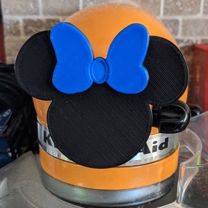 May include: A black and blue 3D printed Mickey Mouse head with a bow, attached to a KitchenAid stand mixer.