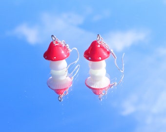 May include: A pair of red and white mushroom-shaped earrings with silver hooks. The earrings are made of polymer clay and have a glossy finish.