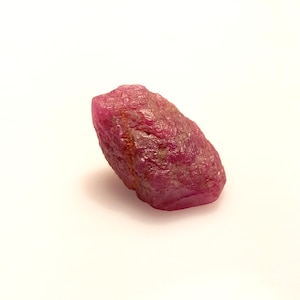 May include: A rough, pink ruby gemstone with a natural, unpolished finish. The ruby has a deep, rich color and is a beautiful example of this precious stone.