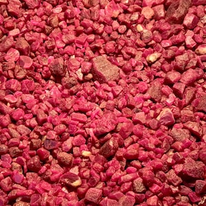 以下が含まれることがあります： ルビーの原石がばらまかれた状態のクローズアップ画像。ルビーは濃い赤色で、形や大きさが様々です。