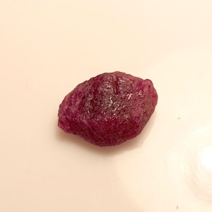 Puede incluir: Una piedra preciosa de rubí rosa oscuro en bruto con una forma irregular natural.