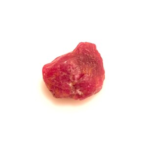 Może przedstawiać: Ciemnoczerwony rubin o surowej, naturalnej powierzchni.