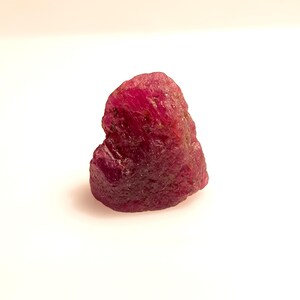 May include: A rough, heart-shaped ruby gemstone with a deep red color.