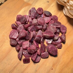 Puede incluir: Un montón de piedras preciosas de rubí rosa en bruto. Los rubíes son de varios tamaños y formas, algunos tienen una forma más puntiaguda y otros son más redondeados.