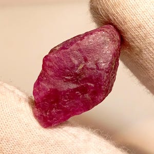 Op de afbeelding: Een dieprode robijn edelsteen met een ruwe, natuurlijke vorm. De robijn wordt in een witte doek gehouden.
