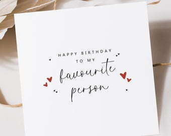 May include: A white greeting card with the text "HAPPY BIRTHDAY TO MY favourite person" in black script. Small red hearts and black accents surround the text. The card is square and sits on a neutral background.
