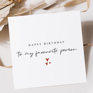 May include: White card with the text "Happy Birthday to my favourite person" in black script. Three small red hearts are below the text.