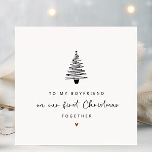 K&ouml;nnte beinhalten: Quadratische Weihnachtskarte mit minimalistischem Design. Die Karte zeigt eine schwarze Strichzeichnung eines Weihnachtsbaums und den Text "TO MY BOYFRIEND on our first Christmas TOGETHER" mit einem kleinen roten Herz.