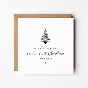 K&ouml;nnte beinhalten: Eine quadratische wei&szlig;e Weihnachtskarte mit braunem Umschlag. Die Karte zeigt eine minimalistische schwarze Strichzeichnung eines Weihnachtsbaums und den Text "TO MY BOYFRIEND on our first Christmas TOGETHER" mit einem kleinen roten Herz.