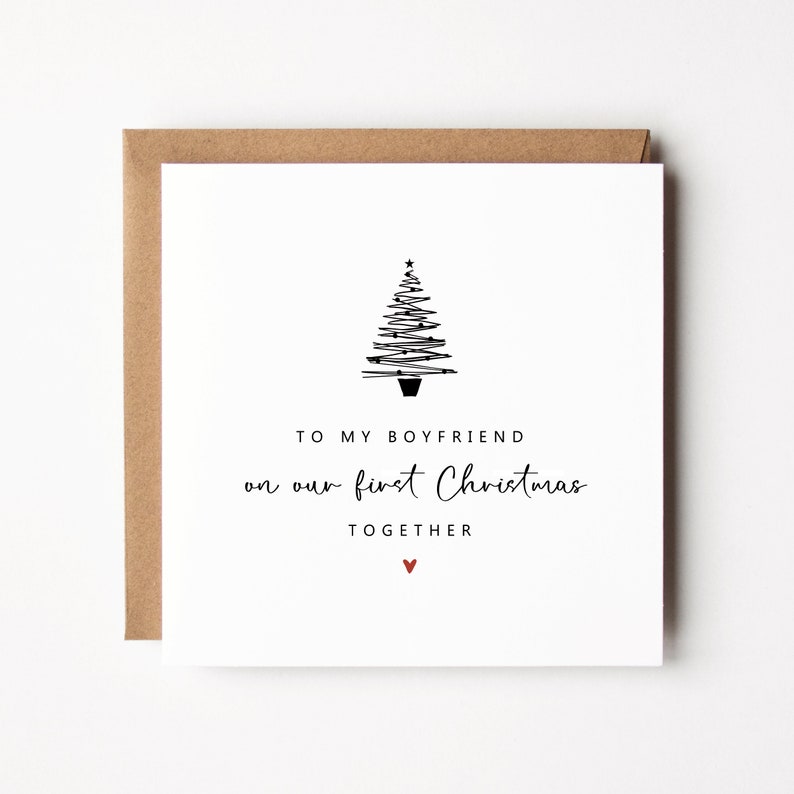 K&ouml;nnte beinhalten: Eine quadratische wei&szlig;e Weihnachtskarte mit braunem Umschlag. Die Karte zeigt eine minimalistische schwarze Strichzeichnung eines Weihnachtsbaums und den Text "TO MY BOYFRIEND on our first Christmas TOGETHER" mit einem kleinen roten Herz.
