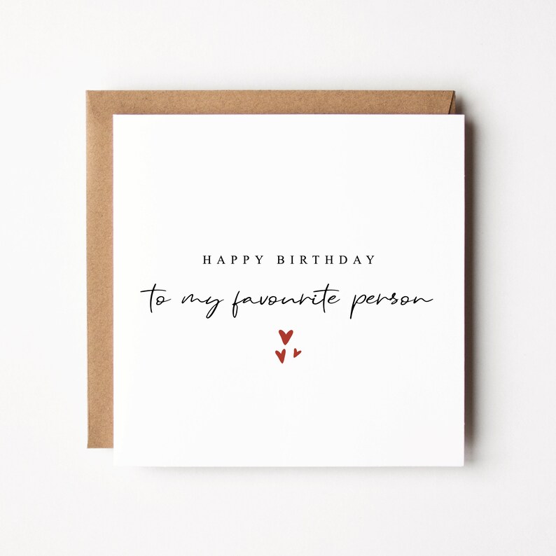 May include: A white card with the text "Happy Birthday to my favourite person" in black script. Three small red hearts are centered below the text.