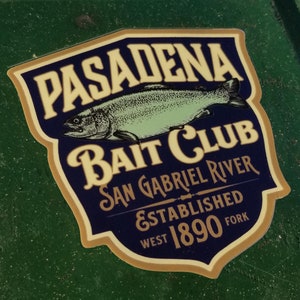 May include: A vintage-style sticker with a blue and gold design. It features a fish, the text "Pasadena Bait Club", and the words "San Gabriel River West Fork Established 1890".