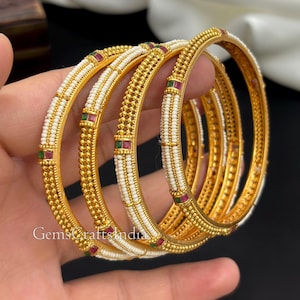 Peut inclure: Un ensemble de quatre bracelets rigides dorés ornés de rangées de petites perles blanches et d'accents rectangulaires rouges et verts alternés. La surface métallique présente un motif perlé texturé sur toute sa longueur.