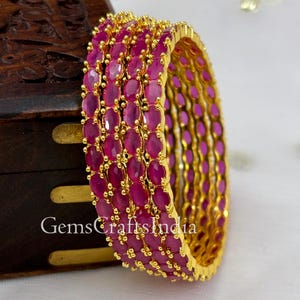 Könnte beinhalten: Satz von vier goldenen Armreifen mit rosafarbenen ovalen Steinen. Jeder Armreif ist mit kleinen goldenen Perlen verziert.