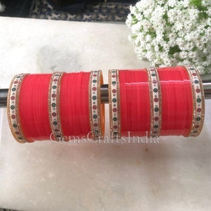 May include: Set of four pink bangles with white and gold decorative accents. The bangles have a design of small circles with black and white centres.