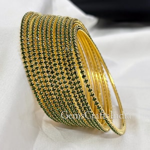 Könnte beinhalten: Ein Stapel goldfarbener Armreifen mit einer Reihe kleiner, quadratischer, dunkelgrüner Edelsteine. Die Armreifen sind in einer gebogenen Form angeordnet, wobei sich einige überlappen. Der Text "GemsCraftsIndia" ist unten rechts sichtbar.